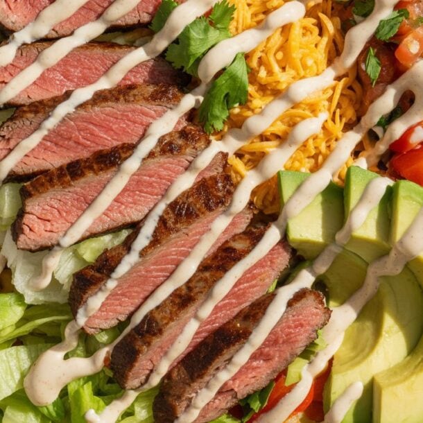 A Chipotle Steak Burrito Bowl filled with sliced grilled steak, shredded cheese, black beans, corn, diced tomatoes, avocado slices, lettuce, and drizzled with creamy dressing—a high-protein meal prep favorite.