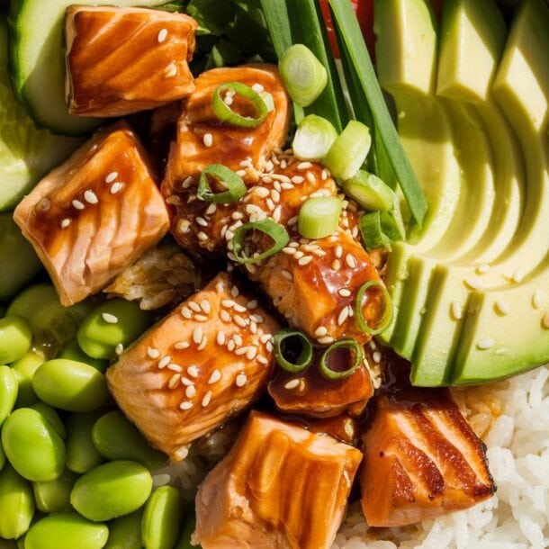 A vibrant rice bowl featuring teriyaki salmon cubes, avocado, cucumber, edamame, green onions, and sesame seeds—perfect for meal prep or a delicious lunch.