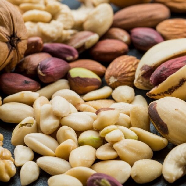 A close-up of assorted healthy nuts, including walnuts, almonds, cashews, pistachios, and peanuts, arranged together on a dark surface.