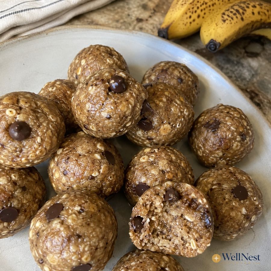 A plate of round oatmeal chocolate chip energy bites, perfect for no-cook meals, sits with ripe bananas in the background; one bite is cut open to reveal the soft texture inside. The WellNest logo is visible in the corner.