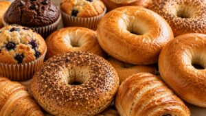 Assorted baked goods including plain and poppy seed bagels, blueberry muffins, chocolate muffins, and flaky croissants arranged closely together—perfect for anyone seeking variety or navigating Zepbound changed taste preferences.